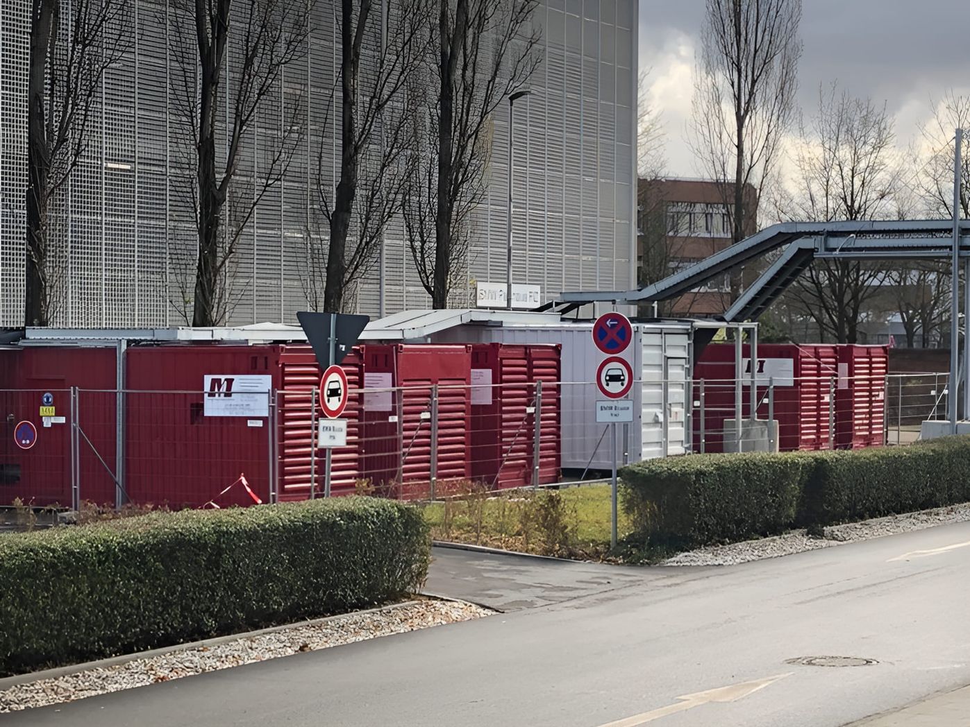 Mobile Notstromaggregate in roten Containern vor einem modernen Gebäude mit Industrieverkleidung